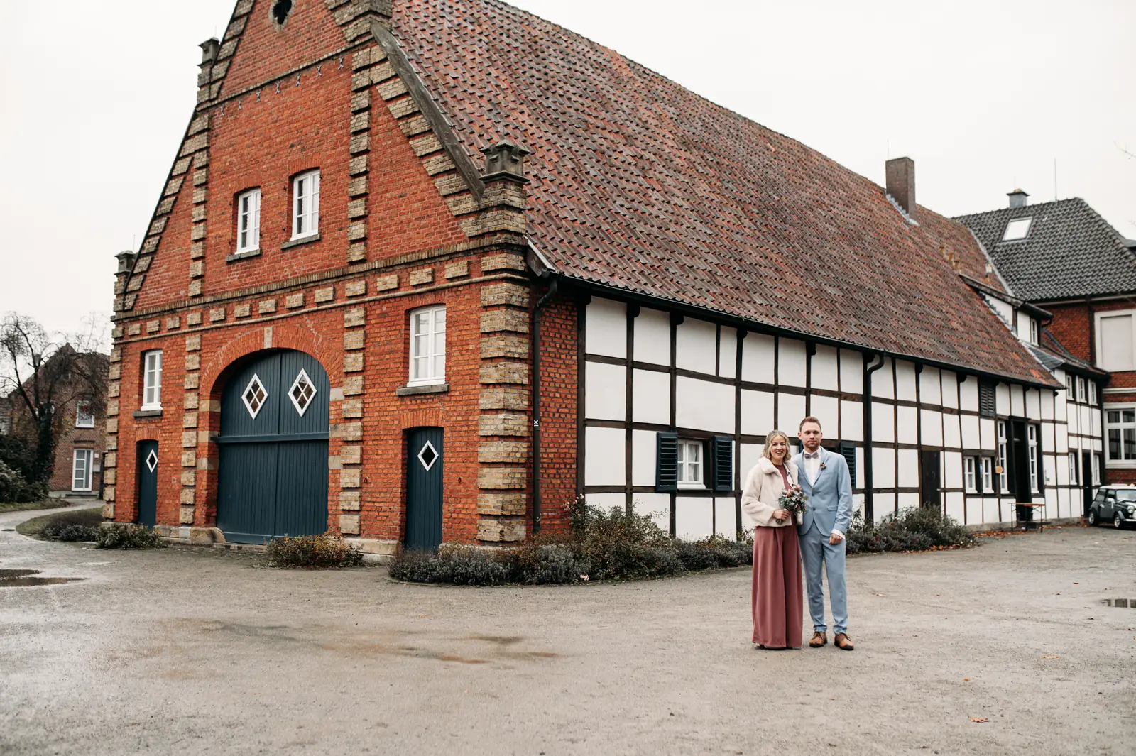Brautpaar steht Hand in Hand vor dem historischen Fachwerk-Torhaus von Haus Siekmann in Sendenhorst