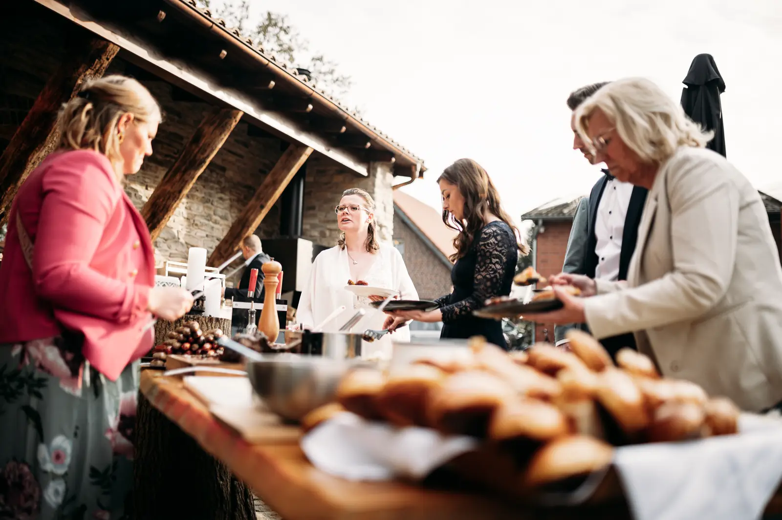 Hochzeitsgäste am rustikalen BBQ-Buffet unter dem Fachwerk-Unterstand von Hof Vincke Ibérico Westfalia in Alverskirchen