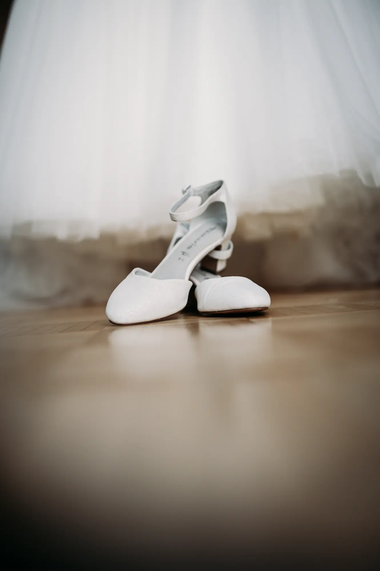 Brautschuhe stehen bereit, im Hintergrund verschwommen das Brautkleid beim Getting Ready