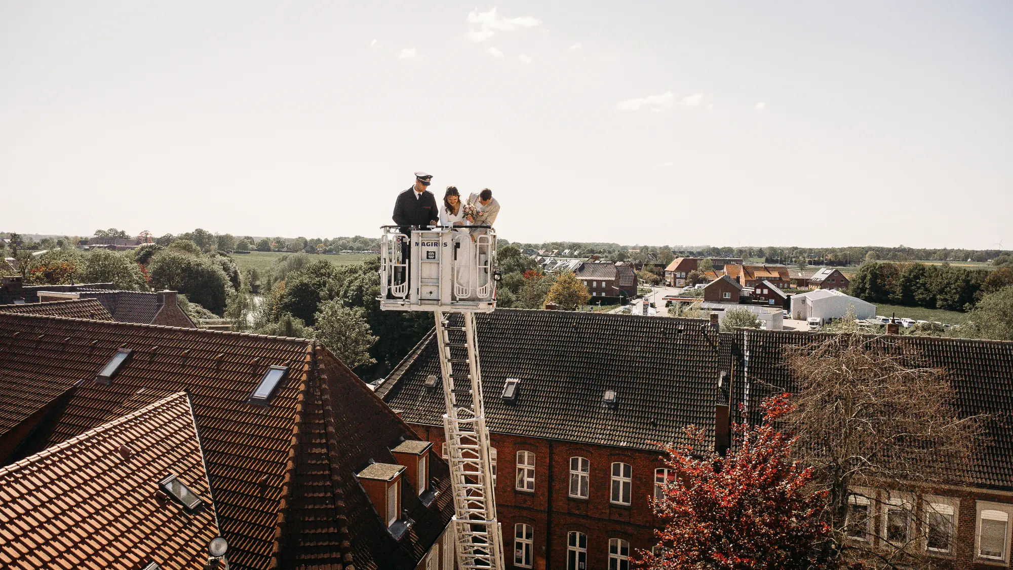 Markus und Kristin genießen mit einem Feuerwehrmann den Ausblick aus dem Korb der Drehleiter hoch über den Dächern von Albersloh