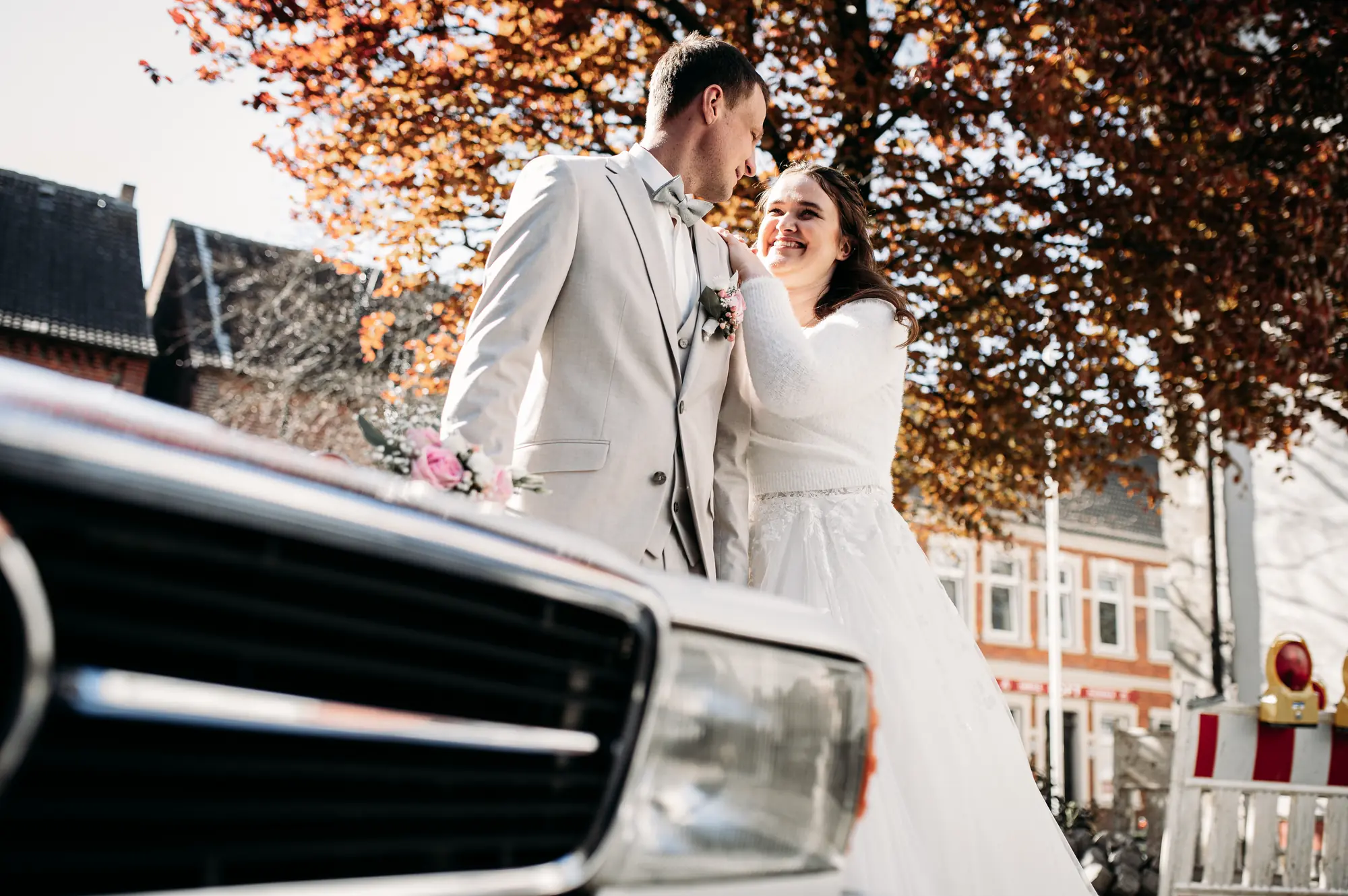 Markus und Kristin auf dem Hochzeitsauto vor einer rot gefärbten Blutbuche