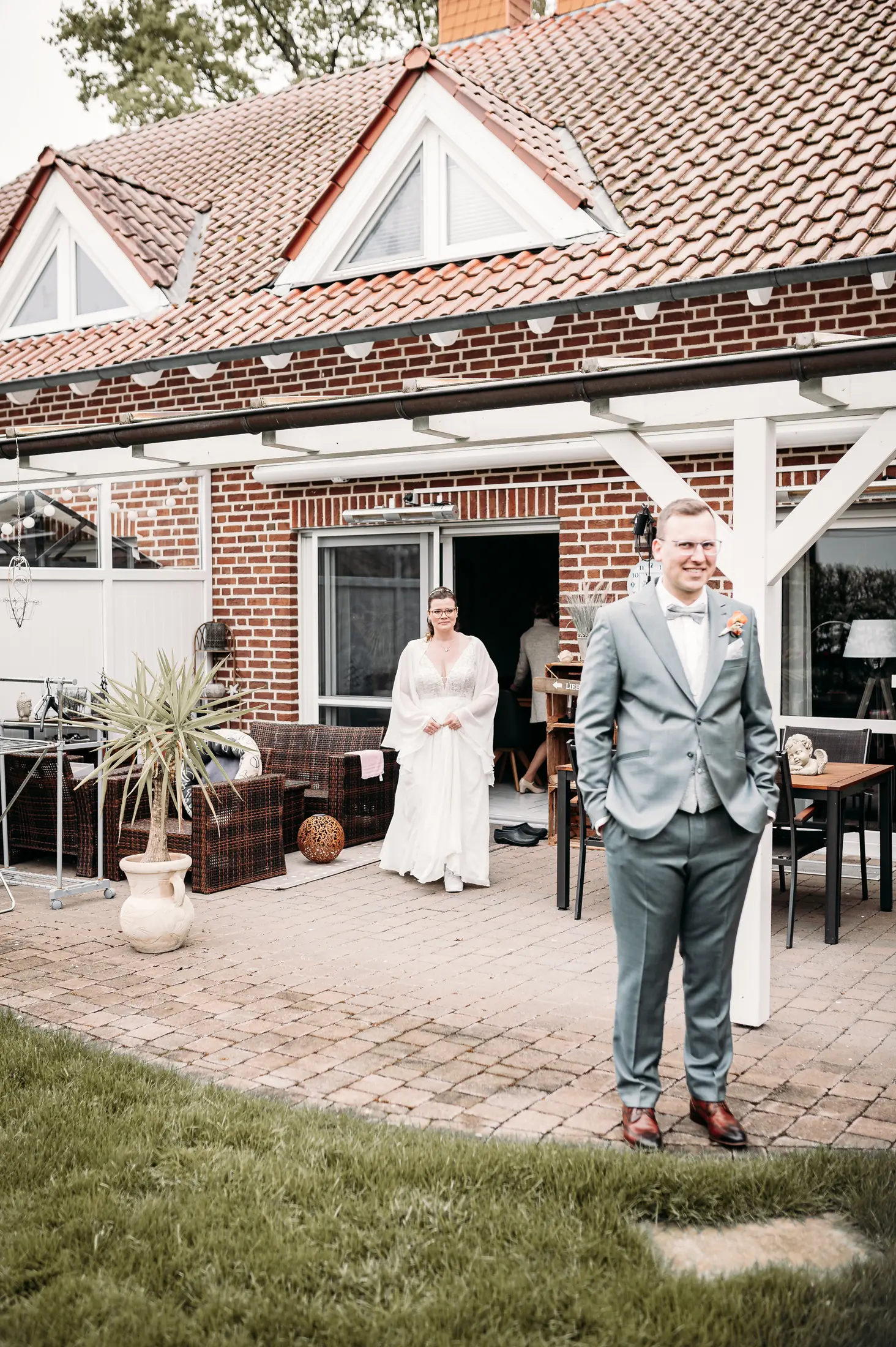 Jannik wartet lächelnd im Garten, während Marina im Brautkleid aus dem Haus tritt – Moment vor dem First Look