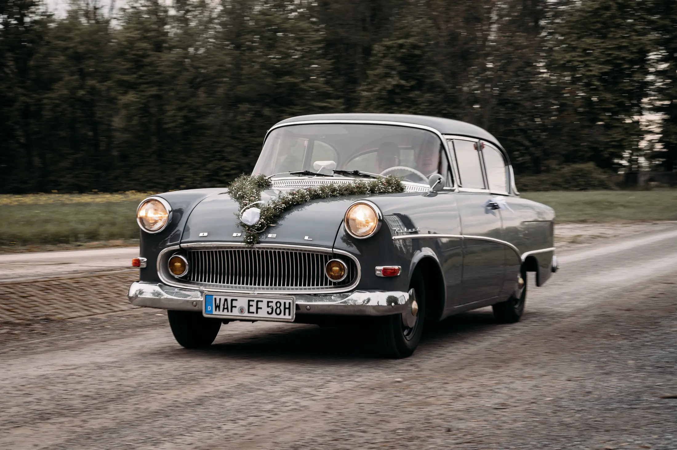 Ein mit Grün geschmücktes Opel-Oldtimer-Hochzeitsauto ist unterwegs zur nächsten Station des Tages