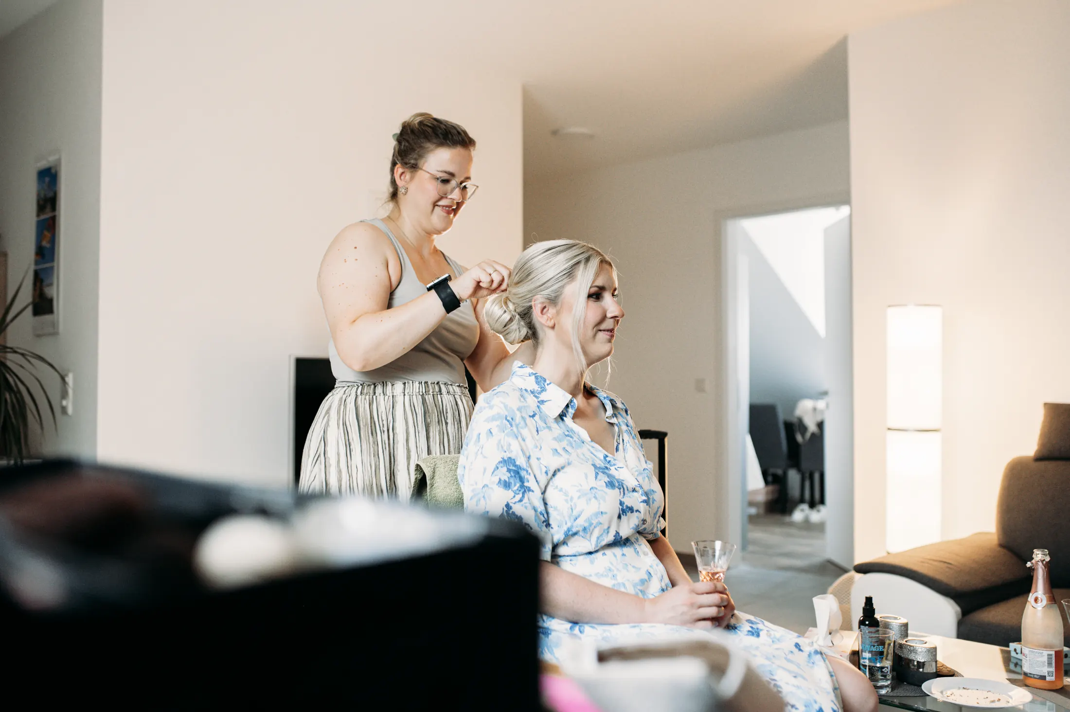 Eine Freundin steckt Viktorias Haare hoch, im Vordergrund ein Glas Sekt beim Getting Ready