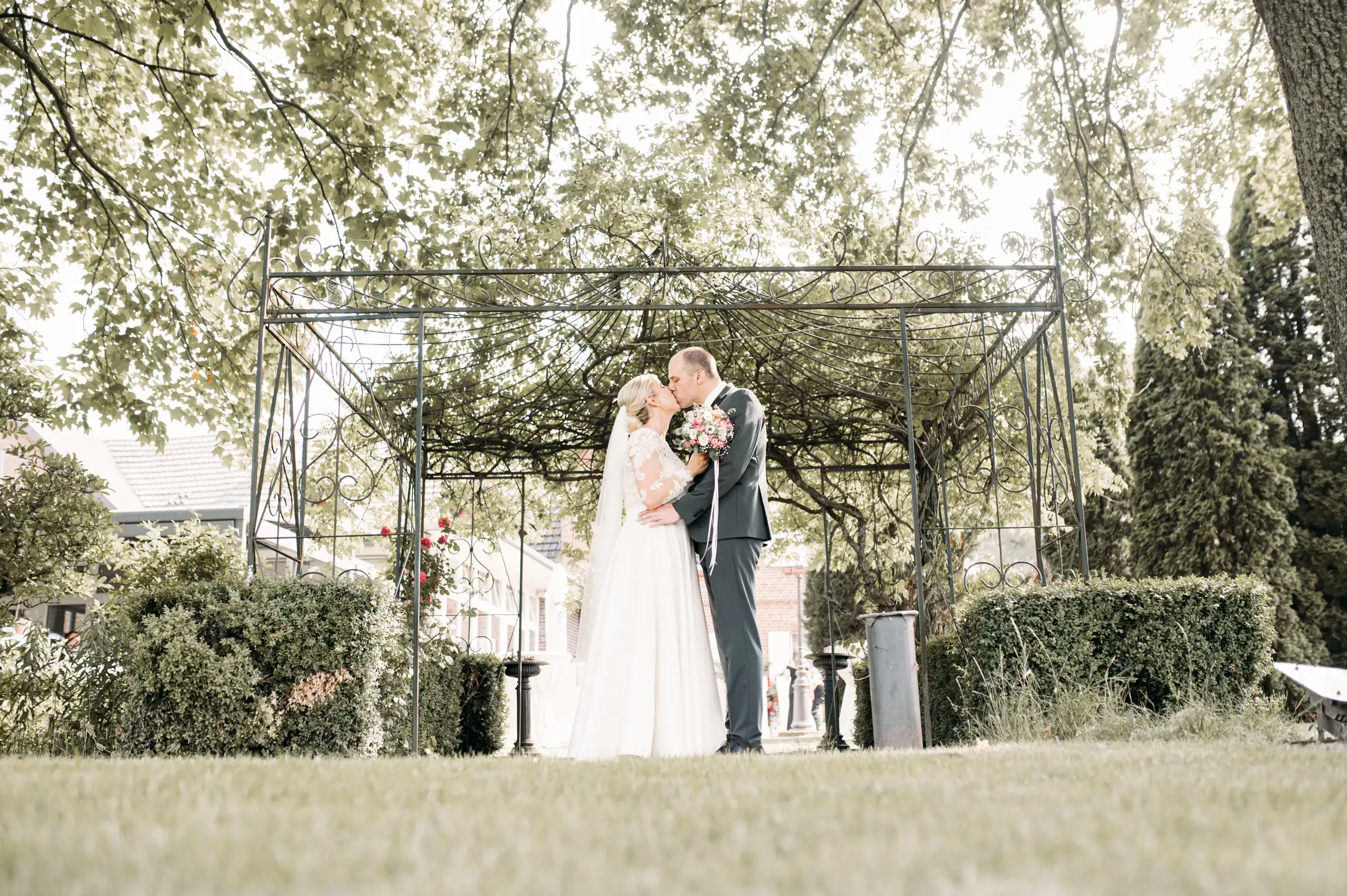 Viktoria und Tobias küssen sich unter der efeuberankten Pergola im Garten von Restaurant Waldmutter